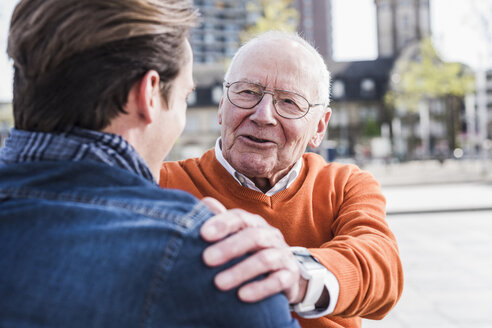 Lächelnder älterer Mann betrachtet seinen erwachsenen Enkel im Freien - UUF10448