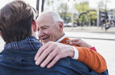 Smiling senior man looking at adult grandson outdoors - UUF10449