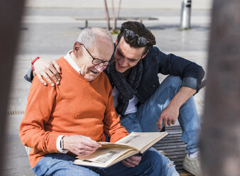 Senior man and adult grandson on a bench looking at photo album - UUF10451