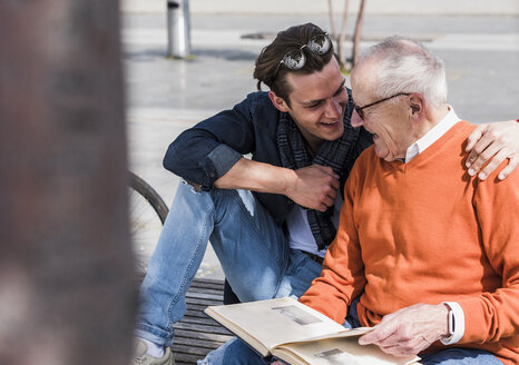 Happy senior man and adult grandson with photo album outdoors - UUF10452