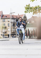 Lächelnder junger Mann mit Fahrrad in der Stadt schaut auf sein Handy - UUF10466