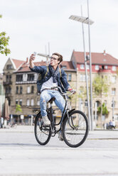Playful young man with bicycle in the city using cell phone - UUF10467