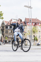 Verspielter junger Mann mit Fahrrad in der Stadt, der ein Mobiltelefon benutzt - UUF10467