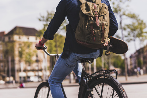 Young man holding skateboard riding bicycle in the city stock photo