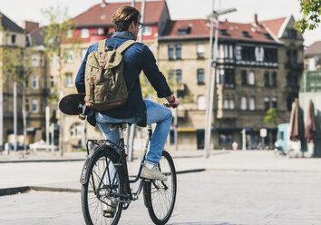 Junger Mann mit Skateboard auf dem Fahrrad in der Stadt - UUF10471