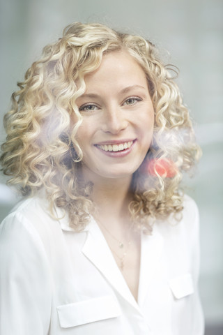 Porträt einer lächelnden blonden Geschäftsfrau hinter einer Fensterscheibe, lizenzfreies Stockfoto