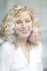 Portrait of smiling blond businesswoman behind windowpane - PESF00520