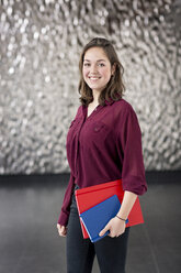 Porträt einer lächelnden jungen Geschäftsfrau mit Notizbüchern in einem Foyer - PESF00530