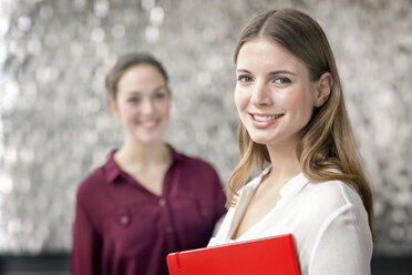 Porträt einer lächelnden jungen Geschäftsfrau mit Notizbuch und Kollegen im Hintergrund - PESF00538