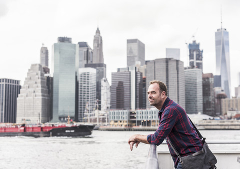 USA, New York City, Mann auf Fähre mit der Skyline von Manhattan im Hintergrund, lizenzfreies Stockfoto