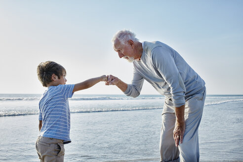 Grandfather giving grandson a fist bump on the beach - RORF00794