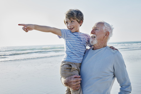 Großvater trägt Enkel am Strand, lizenzfreies Stockfoto