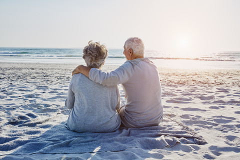 Senior couple sitting on the beach looking at distance stock photo