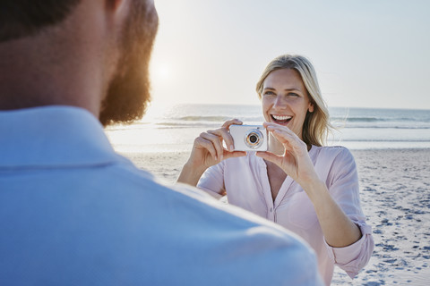 Glückliche Frau, die einen Mann am Strand fotografiert, lizenzfreies Stockfoto