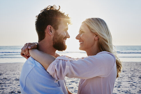 Lächelndes, sich umarmendes Paar am Strand bei Sonnenuntergang - RORF00811