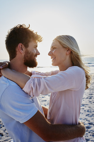 Lächelndes, sich umarmendes Paar am Strand bei Sonnenuntergang, lizenzfreies Stockfoto