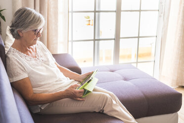 Ältere Frau sitzt auf der Couch und benutzt ein Tablet - SIPF01632