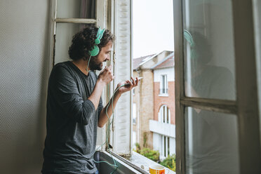 Man talking on cell phone in his room by the window - KIJF01444