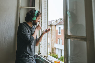 Mann spricht mit Handy in seinem Zimmer am Fenster - KIJF01444