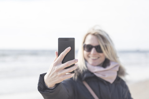 Frau nimmt Selfie mit Handy am Strand, lizenzfreies Stockfoto