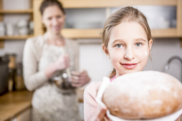 Mädchen hält Brot in der Küche mit Mutter im Hintergrund - WESTF23001