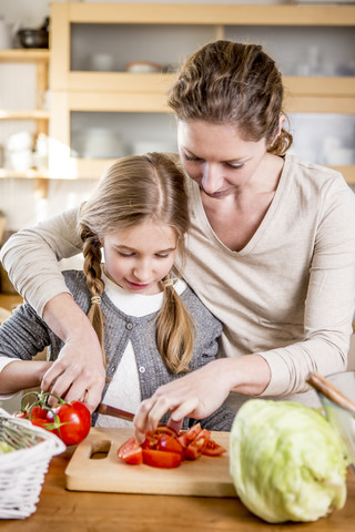 Mutter und Tochter schneiden Tomaten in der Küche, lizenzfreies Stockfoto