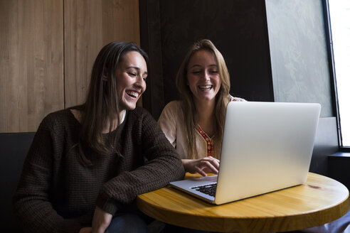 Zwei glückliche Freunde sitzen in einem Café und schauen auf einen Laptop - ABZF01962