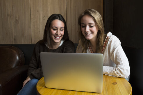 Zwei lächelnde Freunde sitzen in einem Café und schauen auf einen Laptop - ABZF01963