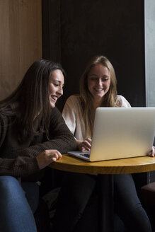 Zwei lächelnde Freunde sitzen in einem Café und schauen auf einen Laptop - ABZF01964