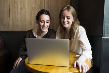 Zwei lächelnde Freunde sitzen in einem Café und schauen auf einen Laptop - ABZF01965