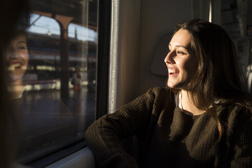 Glückliche junge Frau in einem Zug, die aus dem Fenster schaut - ABZF01977