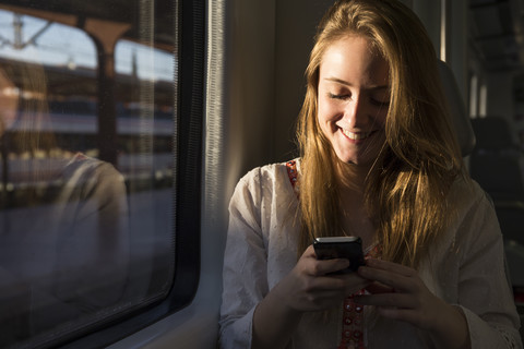 Smiling young woman on a train looking at cell phone stock photo