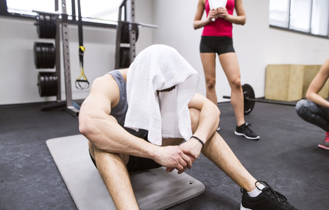 Erschöpfter Sportler mit Handtuch auf dem Kopf nach dem Training im Fitnessstudio, lizenzfreies Stockfoto
