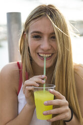 Laughing young woman with yellow beverage - KKAF00727