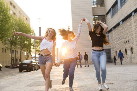 Drei glückliche junge Frauen laufen Hand in Hand auf dem Bürgersteig, lizenzfreies Stockfoto