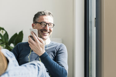 Portrait of smiling businessman using smartphone and earphones - UUF10492