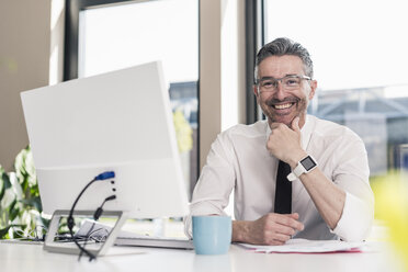 Portrait of smiling businessman sitting at desk in his office - UUF10518