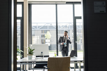 Geschäftsmann mit einer Tasse Kaffee am Telefon in seinem Büro - UUF10530