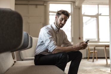 Portrait of young businessman using cell phone in a loft - JOSF00733