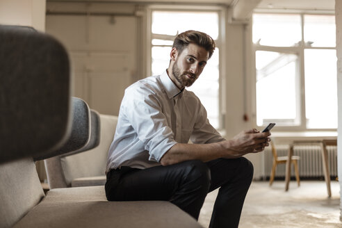 Porträt eines jungen Geschäftsmannes, der in einem Loft ein Mobiltelefon benutzt - JOSF00733