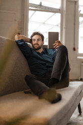 Portrait of young freelancer sitting on the couch with tablet - JOSF00735