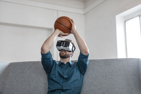 Junger Mann mit Basketball auf der Couch sitzend mit Virtual Reality-Brille - JOSF00739