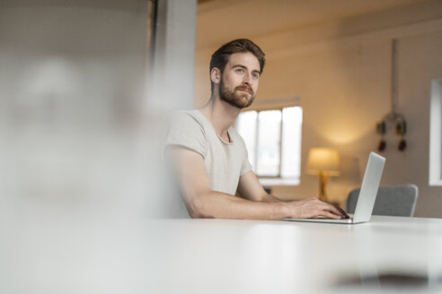 Porträt eines jungen Mannes, der in einem Loft an einem Laptop arbeitet - JOSF00758