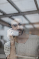 Porträt eines jungen Mannes, der hinter einer Fensterscheibe telefoniert - JOSF00762