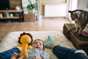 Mother playing with her baby daughter on couch with cats watching - GEMF01602