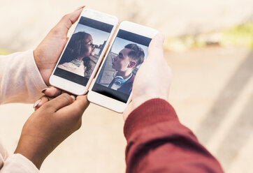 Hands holding smart phones with pictures of a young couple - UUF10532