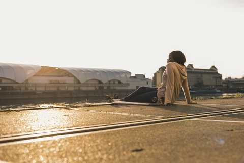 Junge Frau sitzt am Fluss und beobachtet den Sonnenuntergang, lizenzfreies Stockfoto