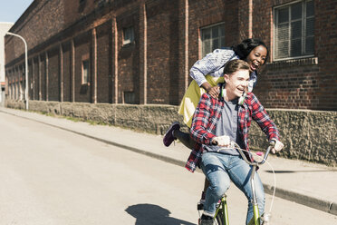 Young man riding bicycle with his girlfriend standing on rack - UUF10544