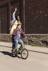 Junger Mann auf dem Fahrrad mit seiner Freundin auf dem Gepäckträger stehend - UUF10547