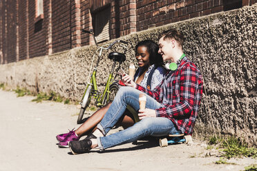 Young couple sitting on ground, eating icecream - UUF10549